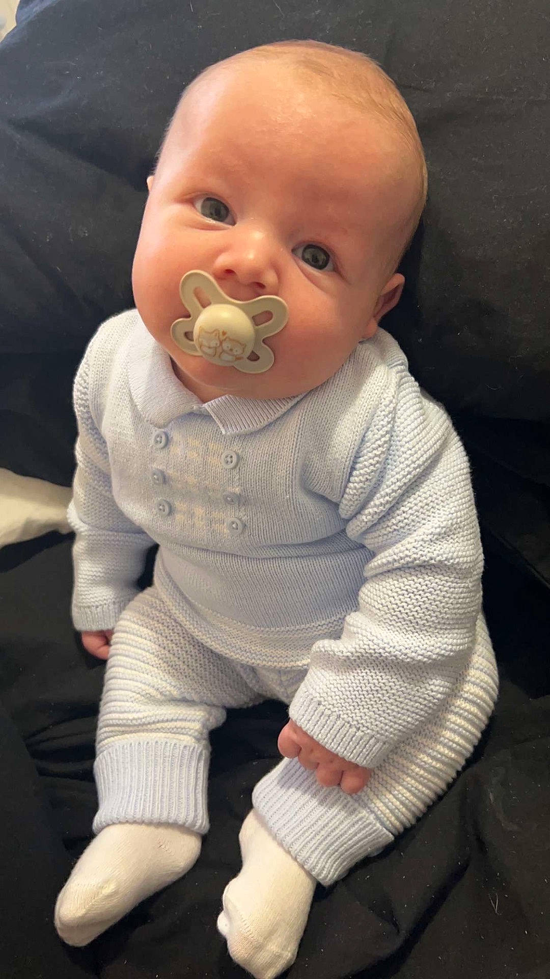 Remy is registered to the contest to win money with this photo: baby, background, casual, child, cozy, curious_expression, cute, indoors, infant, knitted_clothing, light_blue, pacifier, portrait, round_face, sitting, small_hands, soft_texture, warm_clothing, white_socks, young_child