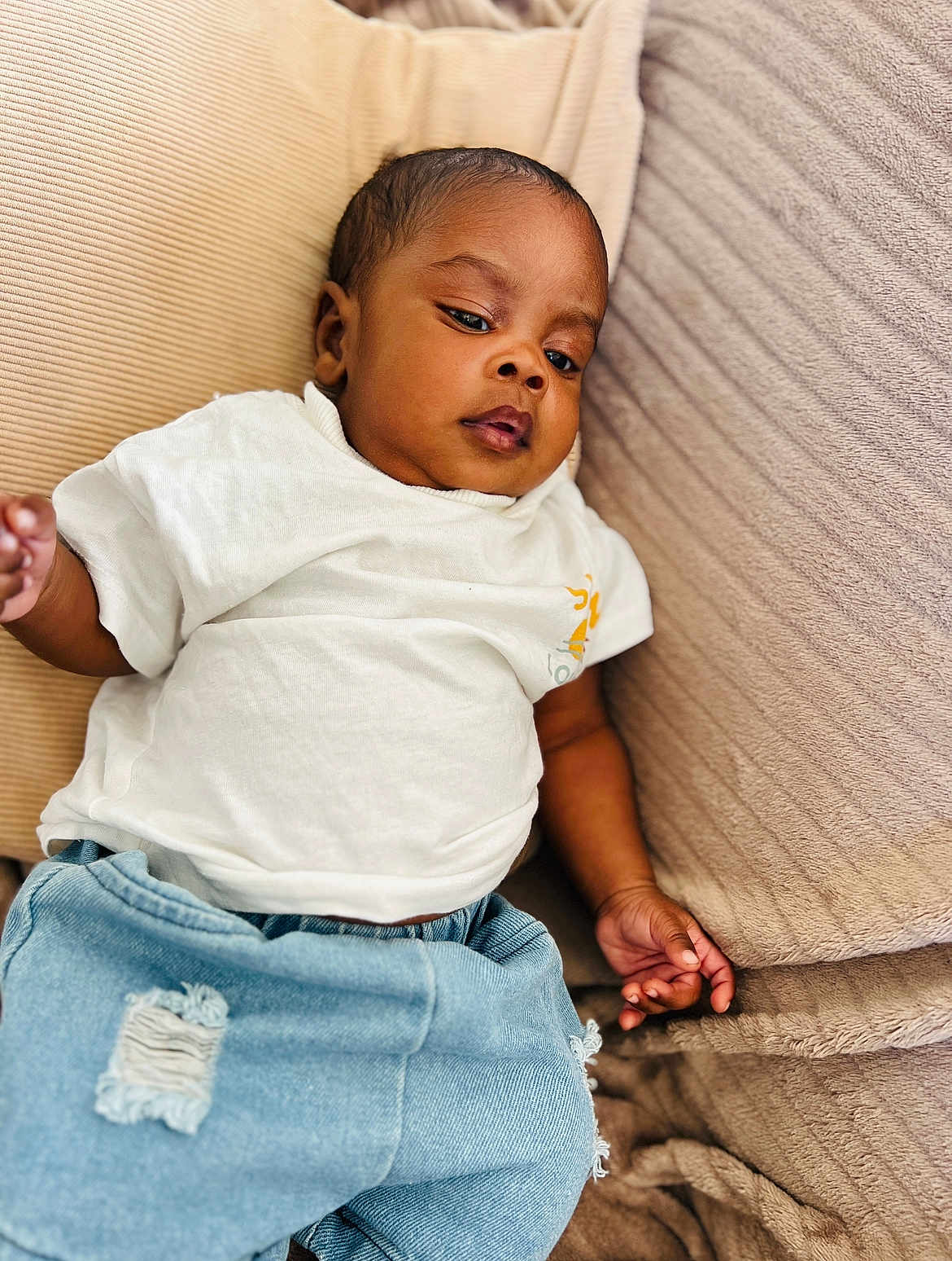 Muhammad a rejoint le concours — aidez-le/la à gagner de superbes lots ! baby, child, infant, clothing, white_tshirt, blue_jeans, couch, cushion, indoor, relaxed, portrait, person, young_child, casual, cute, skin, face, hand, seated, comfort