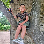 Nöa a rejoint le concours — aidez-le/la à gagner de superbes lots ! boy, camouflage_shirt, casual_clothing, child, daylight, greenery, nature, outdoor, park, playful, recreation, relaxed, shorts, smiling, sneakers, stone_wall, toy_car, tree, tree_branch, young