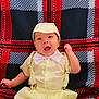 baby, child, yellow_outfit, bow_tie, cap, suspenders, happy, smiling, face, portrait, plaid_blanket, red, black, white, clothing, cute, infant, lying_down, expression, indoors