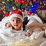 baby, child, santa_hat, christmas_tree, christmas_ornaments, fairy_lights, blanket, holiday, festive, smiling, cute, indoors, decorations, red, green, white, plaid, face, person, celebration