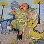 Yujin is registered to the contest to win money with this photo: baby, infant, smiling, dinosaur, blanket, green_clothing, footwear, cute, happy, lying_down, indoor, child, patterned_clothes, playful, cartoon, animal_print, toddler, soft_toys, youth, small_person