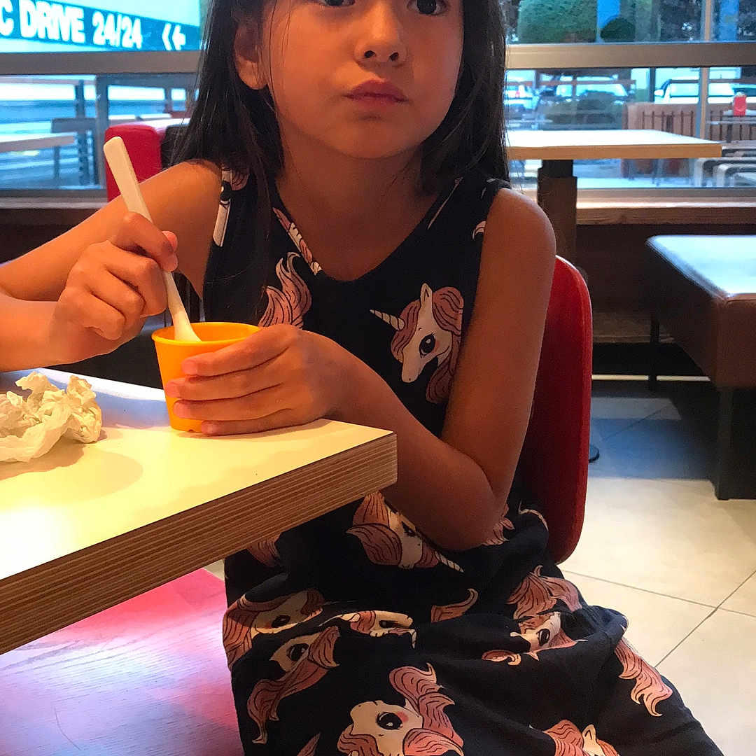 Yuna Lepertel participe au concours pour gagner de l'argent avec cette photo : cafe, casual_clothing, child, contemplative, cute, daylight, food, girl, indoor, person, red_chair, relaxed, sitting, snack, spoon, table, unicorn_dress, window, yellow_cup, young