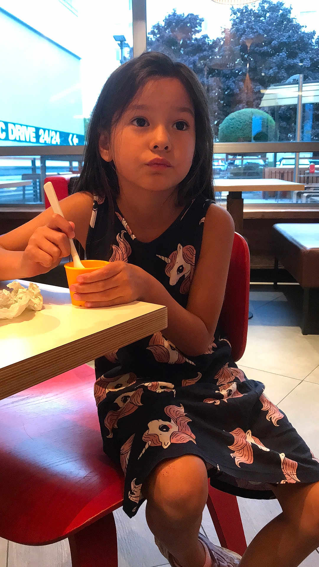 Yuna Lepertel participe au concours pour gagner de l'argent avec cette photo : child, girl, unicorn_dress, red_chair, yellow_cup, spoon, indoor, cafe, table, snack, food, window, daylight, casual_clothing, sitting, contemplative, young, person, cute, relaxed
