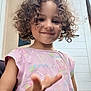 child, curly_hair, smile, pink_shirt, outdoor, door, hand, sea_creatures, starfish, seahorse, playful, young, person, casual_clothing, expression, portrait, front_view, daylight, happy, skin