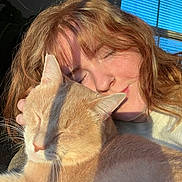Chef Boyardee is registered to the contest to win money with this photo: person, cat, pet, animal, indoor, sunlight, window, blinds, face, hair, feline, close_up, snuggling, cozy, relaxed, eyes_closed, warm_light, shadow, nose_ring, soft_fur