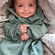 Naima a rejoint le concours — aidez-le/la à gagner de superbes lots ! baby, infant, smiling, big_eyes, blanket, hood, wrap, green_outfit, hands, fingers, close_up, portrait, cute, cozy, car_seat, padded_blanket, textured_fabric, soft_material, seat_strap, adorable