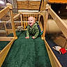 candid, carpet, casual_clothing, child, crawling, cute, fun, green_hoodie, happy, indoor, kid, person, play_area, plush_toy, smiling, toddler, toy, wooden_play_structure, wooden_walls, young_child