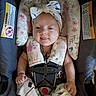 baby, infant, car_seat, headband, flower_pattern, pacifier, smile, tongue_out, sitting, straps, clothing, cute, child, indoors, fabric, safety_harness, person, playful, young, seat