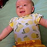 Eloise is registered to the contest to win money with this photo: baby, infant, smiling, lying_down, yellow_clothing, lemon_pattern, onesie, cute, happy, child, face, cheerful, portrait, indoors, soft_surface, playful, skin, head, young, person
