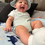 Armani joined the competition — help win amazing prizes! baby, child, hat, onesie, blanket, dinosaur_pattern, smile, laughing, face, hand, foot, socks, couch, pillow, indoor, cute, happy, infant, clothing, portrait