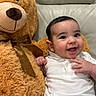 baby, teddy_bear, couch, smile, child, plush_toy, white_shirt, striped_pants, happy, indoor, cute, infant, furniture, cozy, soft_toy, portrait, sitting, light_gray, bow, fun