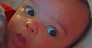 Derrick is registered to the contest to win money with this photo: baby, infant, child, portrait, wide_eyed, lying_down, bed, blanket, pillow, indoors, face, head, eyes, nose, mouth, red_clothing, soft_lighting, close_up, cozy, photography
