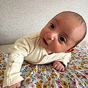 Adam participe au concours pour gagner de l'argent avec cette photo : baby, infant, face, eyes, hand, onesie, blanket, floral_pattern, bed, wall, portrait, close_up, curious, lying_down, skin, gaze, newborn, room_interior, cozy, cute