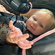 Briella is registered to the contest to win money with this photo: baby, child, car_seat, blue_eyes, blonde_hair, smiling, reaching_hand, safety_harness, infant, cute, portrait, close_up, child_seat, car_interior, black_fabric, pink_trim, happy, young_child, human, seatbelt