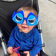Jordan is registered to the contest to win money with this photo: toddler, child, sunglasses, blue, shark, stroller, outdoor, smiling, candy, shorts, jacket, playful, cute, seatbelt, grass, concrete, hand, face, fun, summer