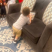 Morgan is registered to the contest to win money with this photo: beige_pants, book, carpet, child, clothing, couch, curly_hair, furniture, gray_shirt, group, home, indoor, kids, living_room, patterned_rug, pillow, reading, shoes, socks, toddler