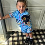 Morgan Xavier is registered to the contest to win money with this photo: toddler, child, smiling, curly_hair, blue_clothing, cartoon_outfit, kitchen, sink, cabinet, snack_bowl, black_shoes, white_socks, checkered_rug, wood_floor, granite_countertop, indoor, standing, happy, person, home