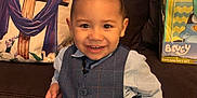 Morgan Xavier is registered to the contest to win money with this photo: toddler, child, smiling, blue_vest, shirt, couch, pillow, gift_set, indoor, happy, portrait, person, curly_hair, buttoned_vest, toy, colorful, seated, young_child, home, casual