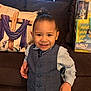 toddler, child, smiling, blue_vest, shirt, couch, pillow, gift_set, indoor, happy, portrait, person, curly_hair, buttoned_vest, toy, colorful, seated, young_child, home, casual