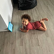 Morgan Xavier is registered to the contest to win money with this photo: toddler, child, curly_hair, floor, wooden_floor, tablet, maroon_outfit, smile, indoor, relaxed, black_bag, wall, technology, leaning, barefoot, person, casual, home, playing, young_child