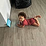 toddler, child, curly_hair, floor, wooden_floor, tablet, maroon_outfit, smile, indoor, relaxed, black_bag, wall, technology, leaning, barefoot, person, casual, home, playing, young_child