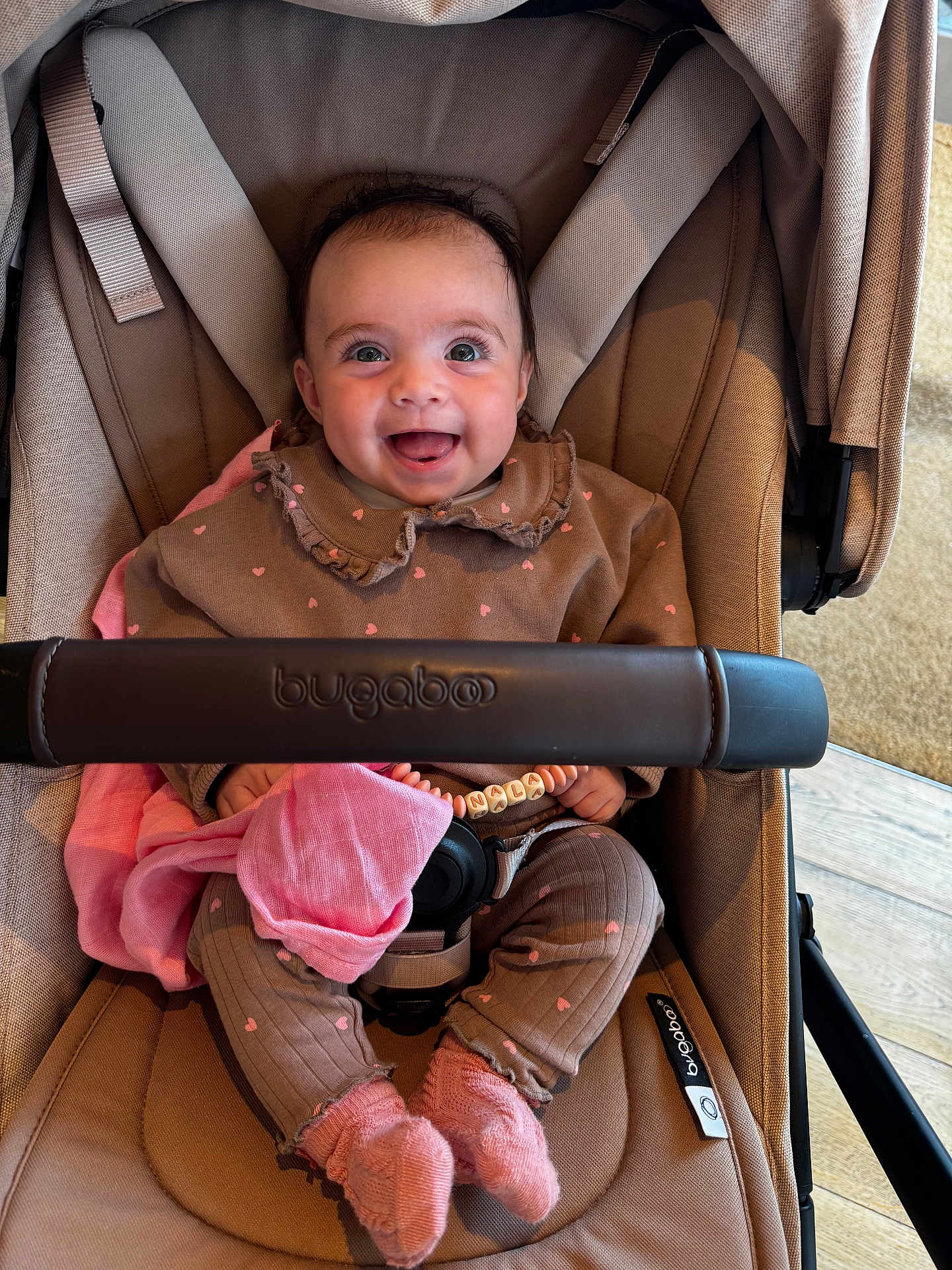Nala is registered to the contest to win money with this photo: baby, child, smiling, stroller, bugaboo, clothing, pink, brown, socks, beads, bracelet, fabric, happy, indoor, seat, person, cute, portrait, infant, toy