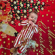 Archie is registered to the contest to win money with this photo: baby, child, pajamas, gingerbread, christmas, holiday, blanket, smile, happy, face, festive, tree, decorations, stars, champagne, glasses, red, white, pattern, lying_down