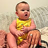 Megan is registered to the contest to win money with this photo: baby, child, yellow_onesie, palm_tree_print, couch, textured_blanket, hand, ring, nail_polish, surprised_expression, indoors, skin, person, sitting, infant, cute, plush_blanket, furniture, portrait, family