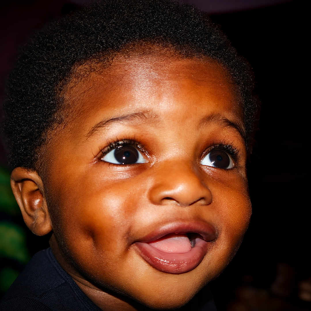 Kieran participe au concours pour gagner de l'argent avec cette photo : baby, child, close_up, curly_hair, cute, dark_background, dimples, expression, eyes, face, happy, head, innocence, joy, mouth, person, portrait, skin, smile, young_child