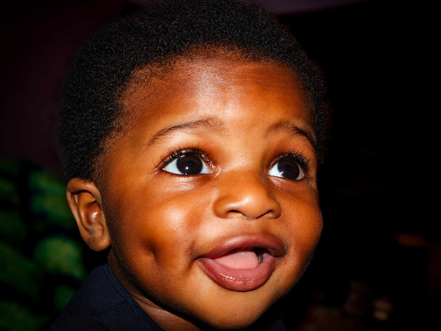 Kieran participe au concours pour gagner de l'argent avec cette photo : child, face, smile, happy, close_up, young_child, dark_background, eyes, mouth, dimples, portrait, curly_hair, skin, expression, person, cute, innocence, joy, head, baby