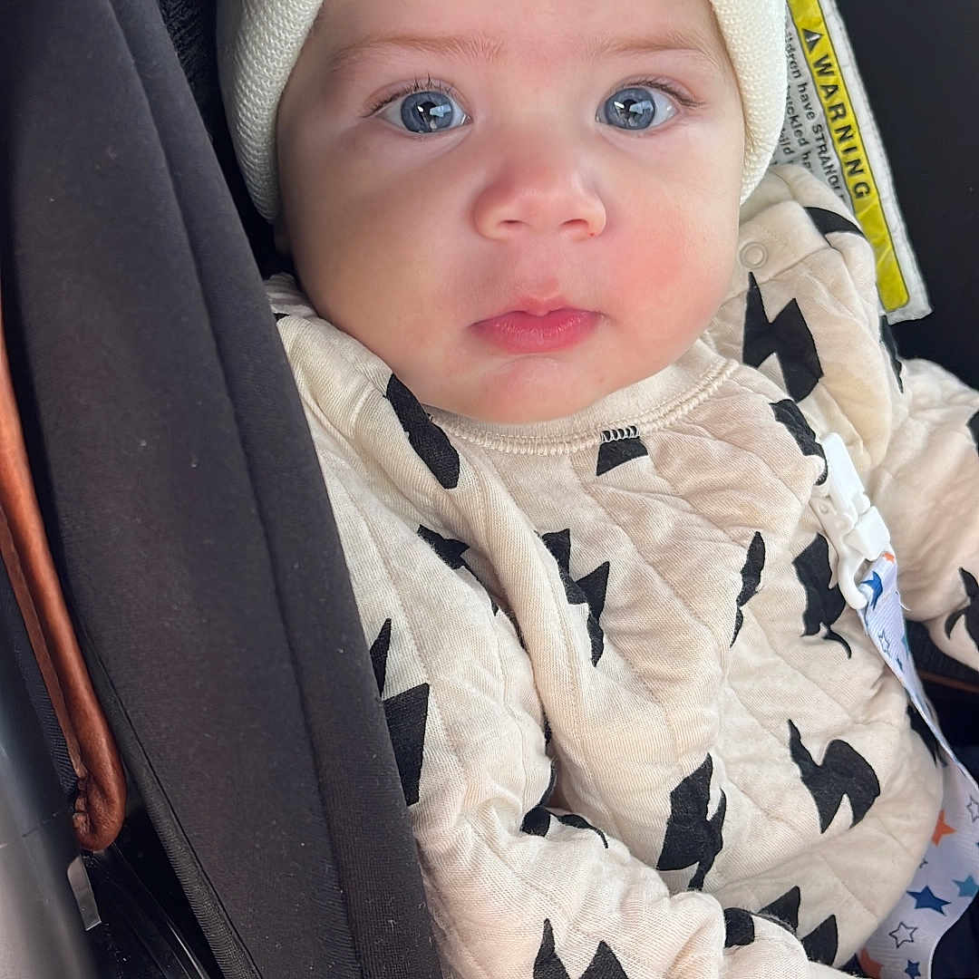 Yaniela is registered to the contest to win money with this photo: adorable, baby, blue_eyes, car_seat, child, close_up, clothing, cute, hat, indoor, infant, newborn, patterned_outfit, person, pom_poms, portrait, safety_harness, seatbelt, winter_wear, young