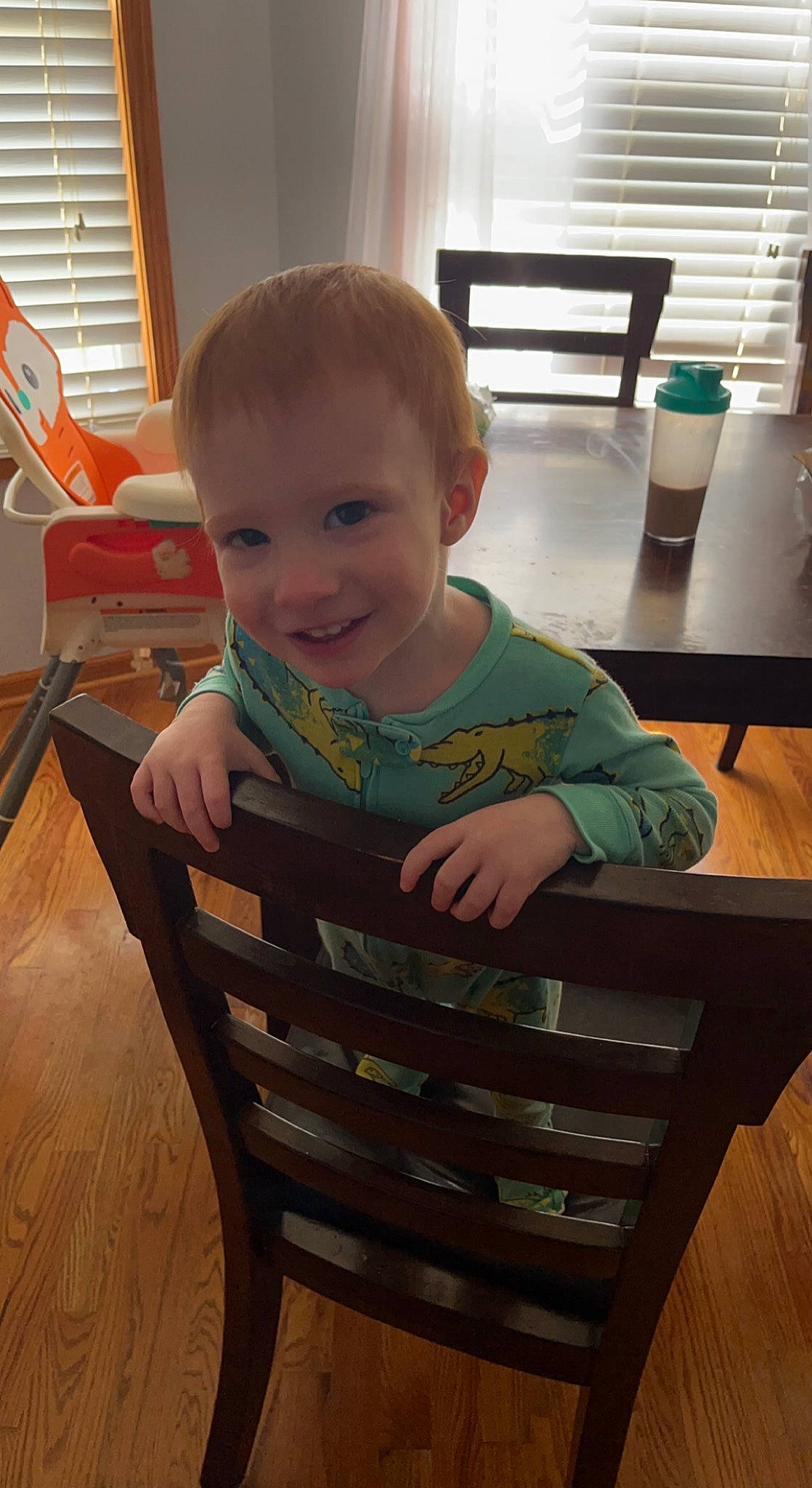Waylon is registered to the contest to win money with this photo: baby_toddler_clothing, chair, cheek, child, comfort, finger, floor, flooring, furniture, green, hardwood, joy, person, smile, standing, table, toddler, varnish, window, window_blind