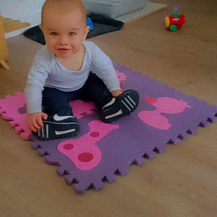 Tyméo a rejoint le concours — aidez-le/la à gagner de superbes lots ! baby, child, clothing, curious, expression, floor, footwear, head, indoor, light, pants, person, plastic_toy, playmat, room, seated, smile, sneakers, toy, young