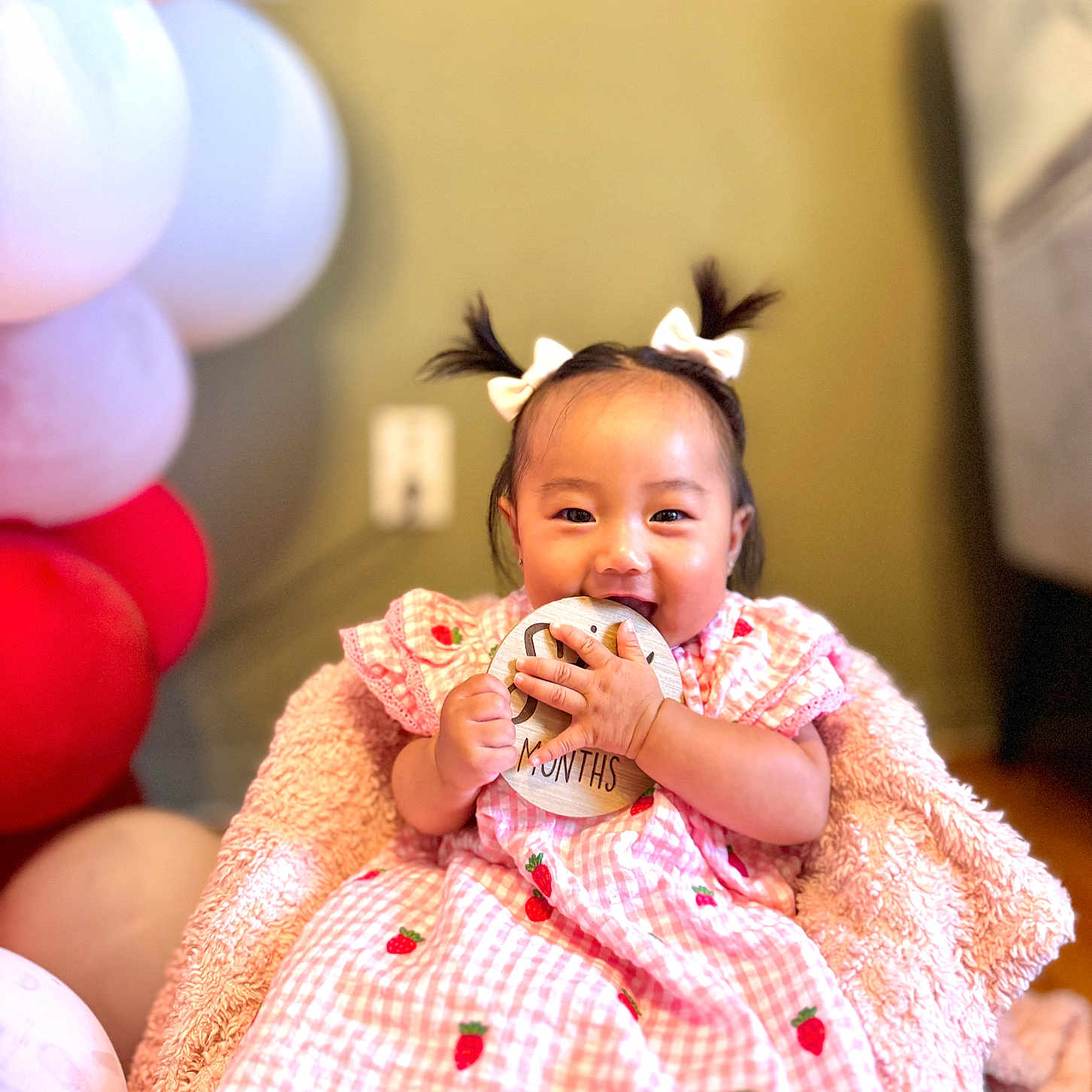 Eleanor is registered to the contest to win money with this photo: baby, balloons, blanket, bows, celebration, child, cute, girl, happy, holding, indoor, infant, pigtails, pink_dress, portrait, sitting, smiling, soft_texture, strawberry_pattern, wooden_sign