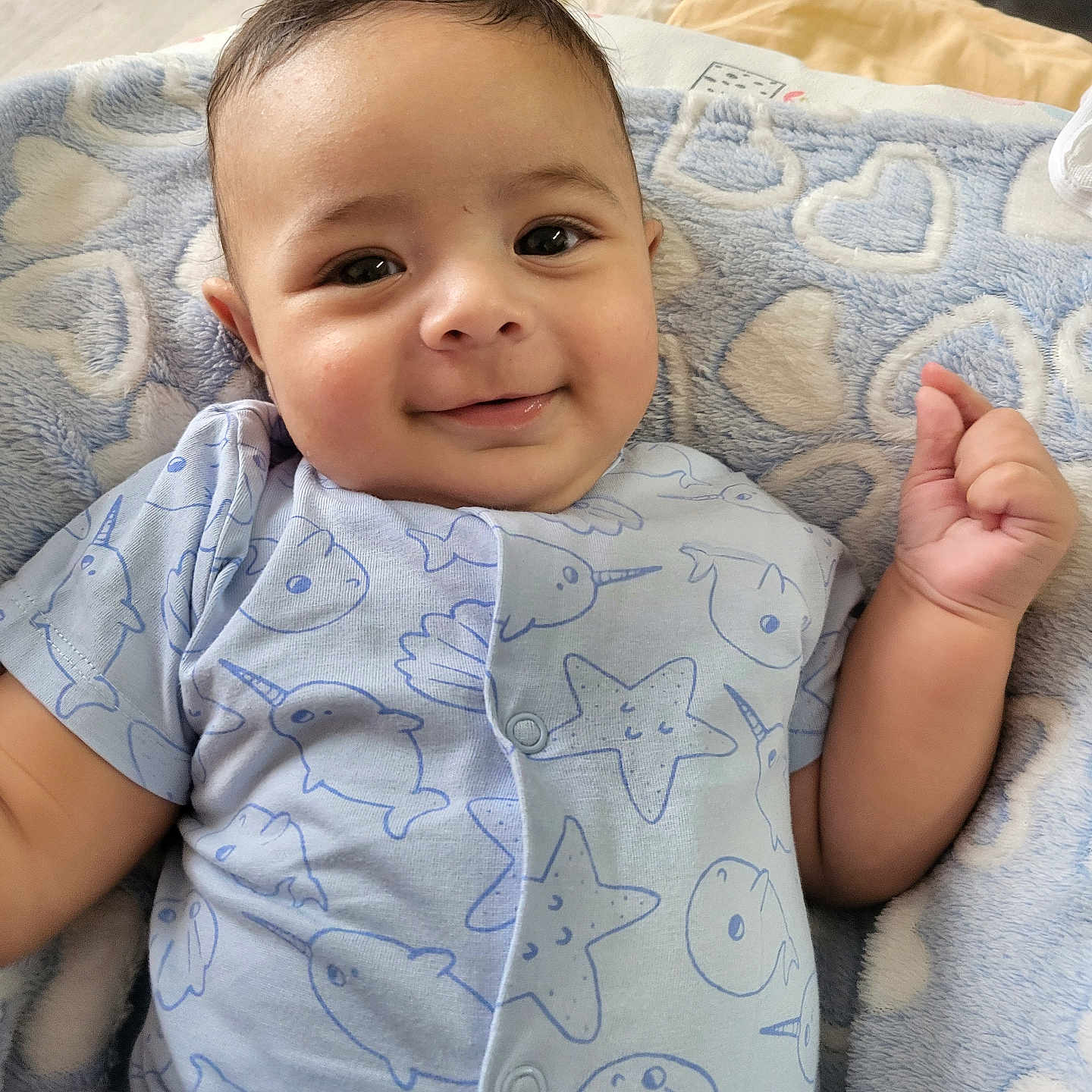 Joao Miguel a rejoint le concours — aidez-le/la à gagner de superbes lots ! baby, blanket, blue_clothing, child, closeup, cozy, cute, face, hand, happy, heart_pattern, home, indoor, infant, lying_down, onesie, person, portrait, smiling, soft_texture