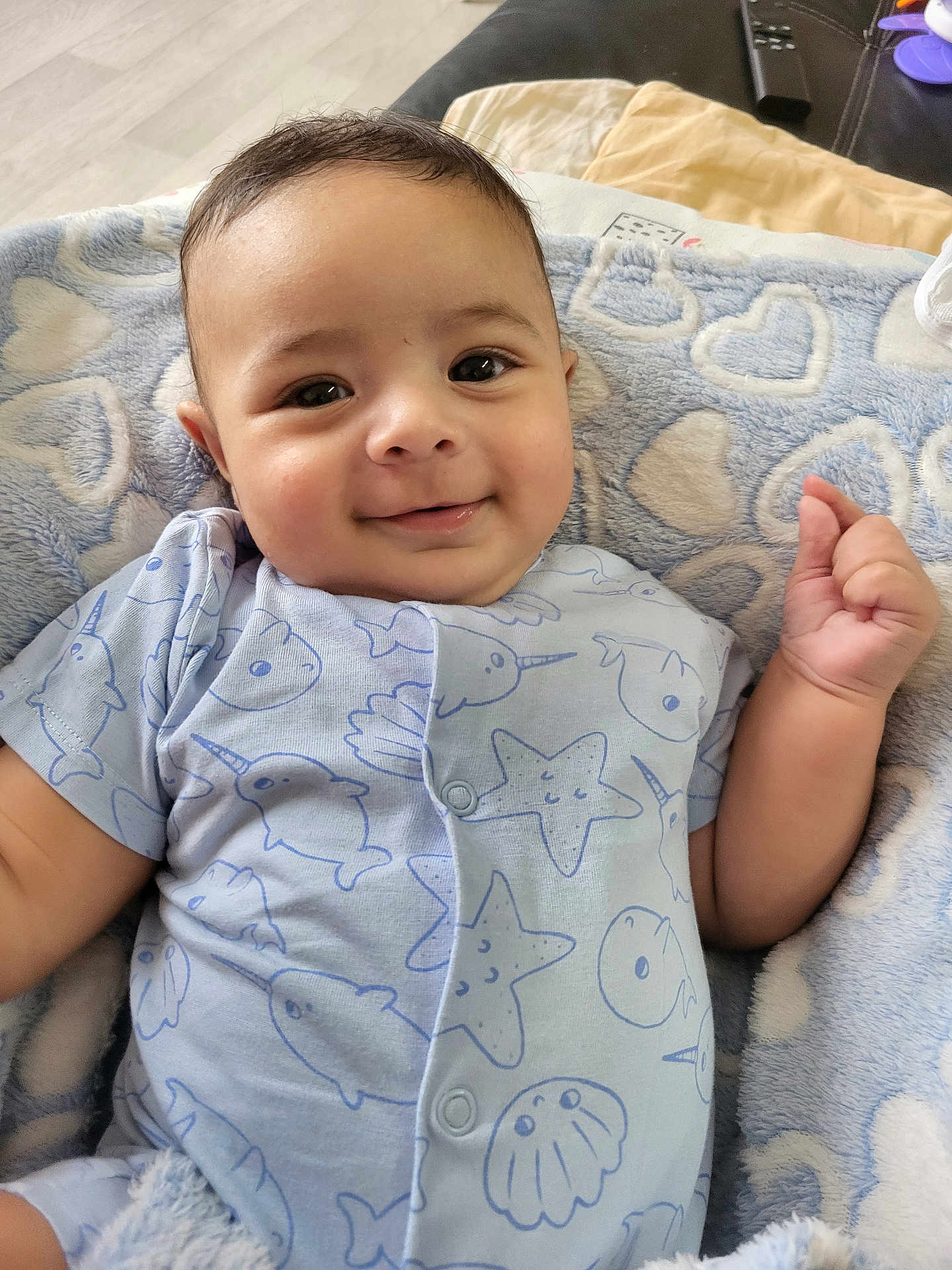 Joao Miguel a rejoint le concours — aidez-le/la à gagner de superbes lots ! baby, smiling, onesie, blue_clothing, blanket, heart_pattern, infant, cute, happy, face, portrait, lying_down, hand, soft_texture, indoor, cozy, child, person, closeup, home