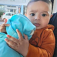 Joao Miguel participe au concours pour gagner de l'argent avec cette photo : baby, child, blanket, orange_sweater, indoor, window, face, hands, curious, person, portrait, soft_texture, cityscape, daylight, seated, closeup, expression, holding, young, casual