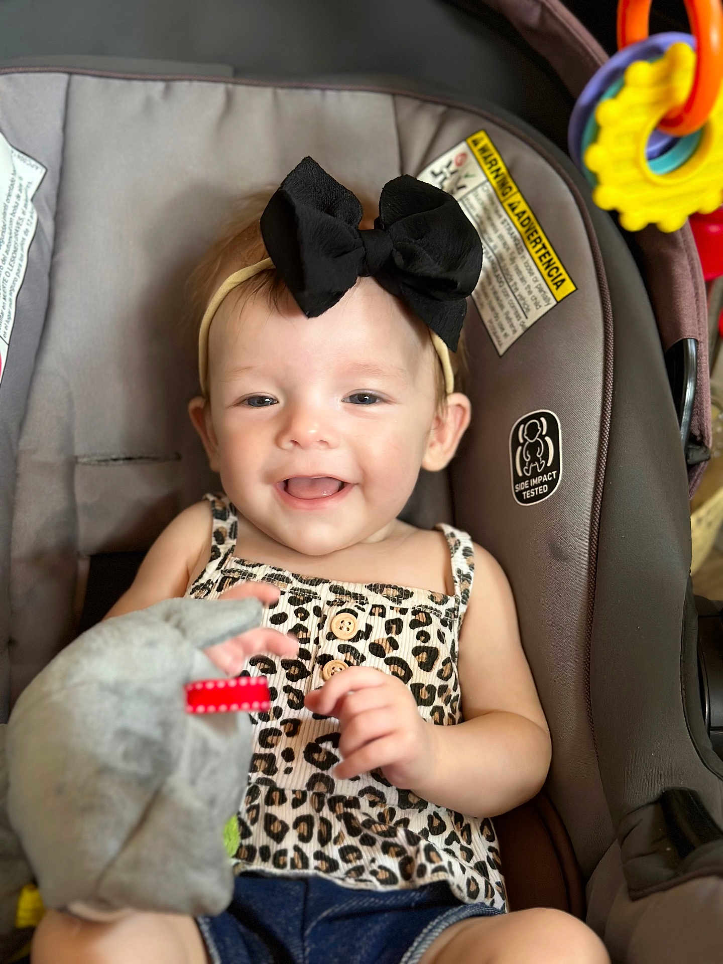 Lillian joined the competition — help win amazing prizes! baby, child, smiling, headband, black_bow, leopard_print, top, denim_shorts, car_seat, toy, soft_toy, hand, happy, infant, cute, indoors, seatbelt, closeup, portrait, playful