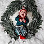 Lucyano a rejoint le concours — aidez-le/la à gagner de superbes lots ! baby, infant, smiling, lying_down, snow, wreath, christmas, hat, striped_pants, red_sock, festive, fur_rug, pine_branches, holiday, cute, portrait, green_clothing, cheerful, seasonal, cozy