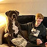 Duke is registered to the contest to win money with this photo: brown_dog, can, casual, couch, dog, furniture, happy, home, hoodie, indoor, lamp, light, male, person, pillow, relaxed, seated, smiling, wall, young_adult