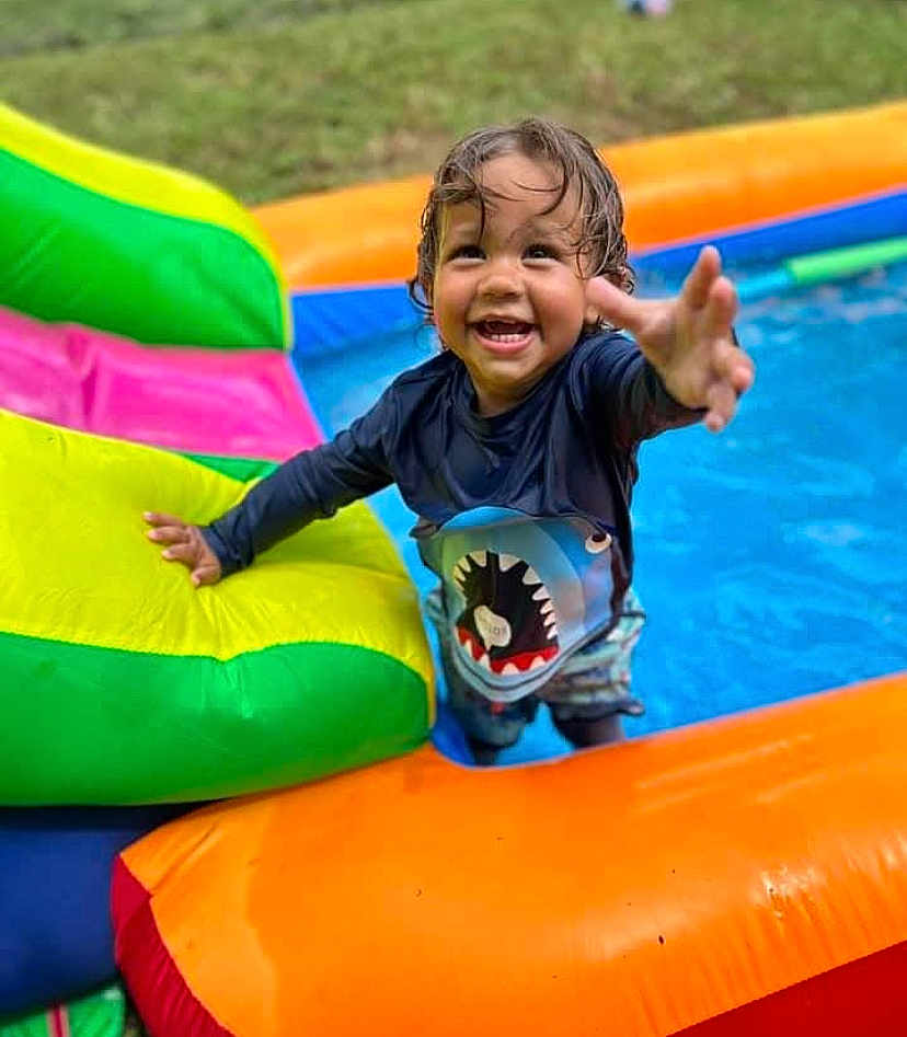 Lorenzo is registered to the contest to win money with this photo: child, toddler, smiling, wet_hair, pool, inflatable_pool, colorful, shark_shirt, water, outdoor, summer, playful, happy, reaching_hand, swimwear, grass, fun, daytime, person, inflatable_toy