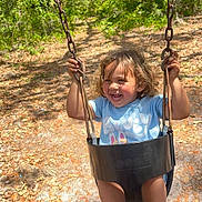 Lorenzo is registered to the contest to win money with this photo: toddler, child, swing, outdoor, forest, trees, sunlight, smiling, happy, playground, rusty_chain, black_swing, curly_hair, blue_shirt, black_shoes, nike, nature, daylight, leaves, joy