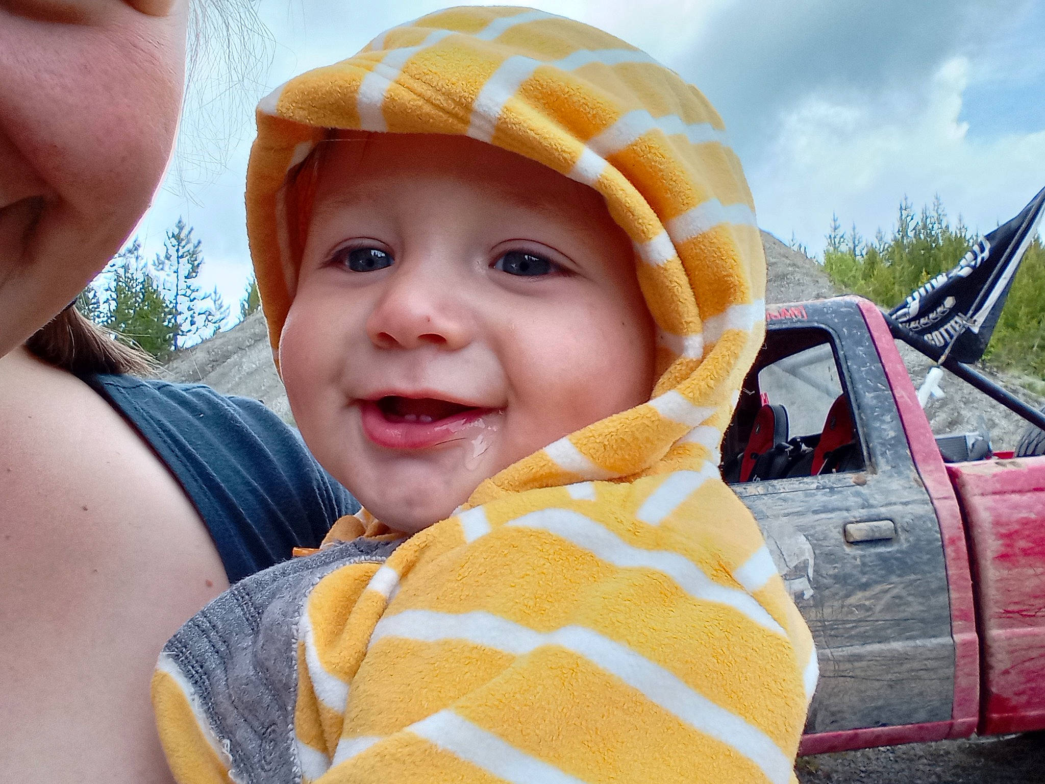 Chevy is registered to the contest to win money with this photo: automotive_tire, baby, cap, car, finger, fun, grass, happy, hat, headwear, hood, joy, leisure, motor_vehicle, person, skin, sky, smile, tire, toddler