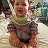 baby, child, red_bow, bib, smiling, sitting, indoors, clothing, cute, happy, infant, face, hands, footwear, sock, bed, fabric, room, mirror, reflection