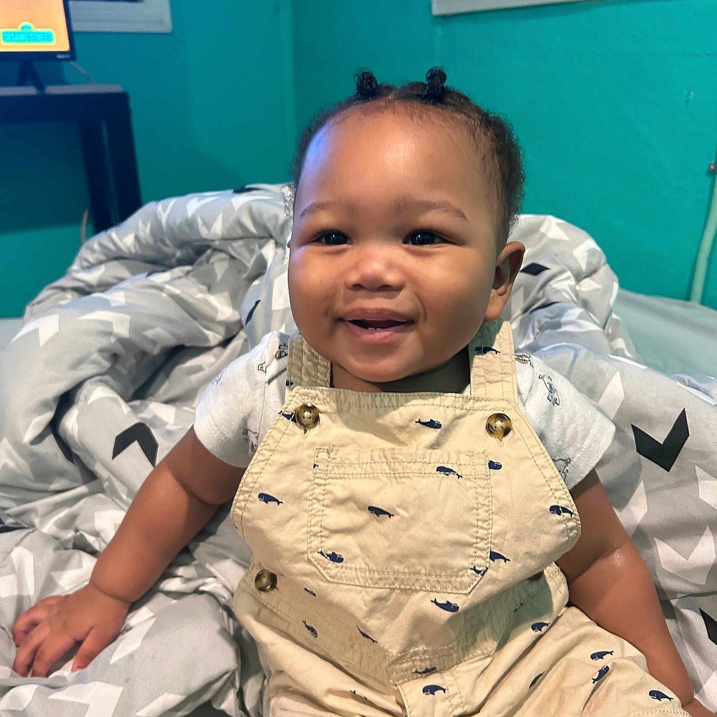 Jamarion joined the competition — help win amazing prizes! toddler, child, smiling, indoors, bed, blanket, overalls, clothing, hair_buns, happy, face, person, room, window, bookshelf, furniture, portrait, casual, skin, cute
