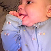 Ryker is registered to the contest to win money with this photo: baby, infant, child, portrait, smiling, happy, sitting, onesie, clothing, hand, fingers, self_soothing, face, eyes, ear, couch, cushion, indoor, cozy, photograph