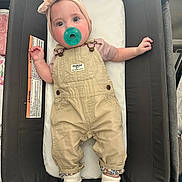 Ivy is registered to the contest to win money with this photo: baby, pacifier, headband, overalls, cushion, baby_seat, infant, clothing, sock, cute, indoor, person, child, face, hand, footwear, fabric, comfortable, looking, resting