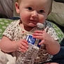 baby, infant, water_bottle, cute, smiling, red_hair, sitting, blanket, pillow, indoor, child, holding, foot, clothing, onesie, person, skin, hand, face, relaxing