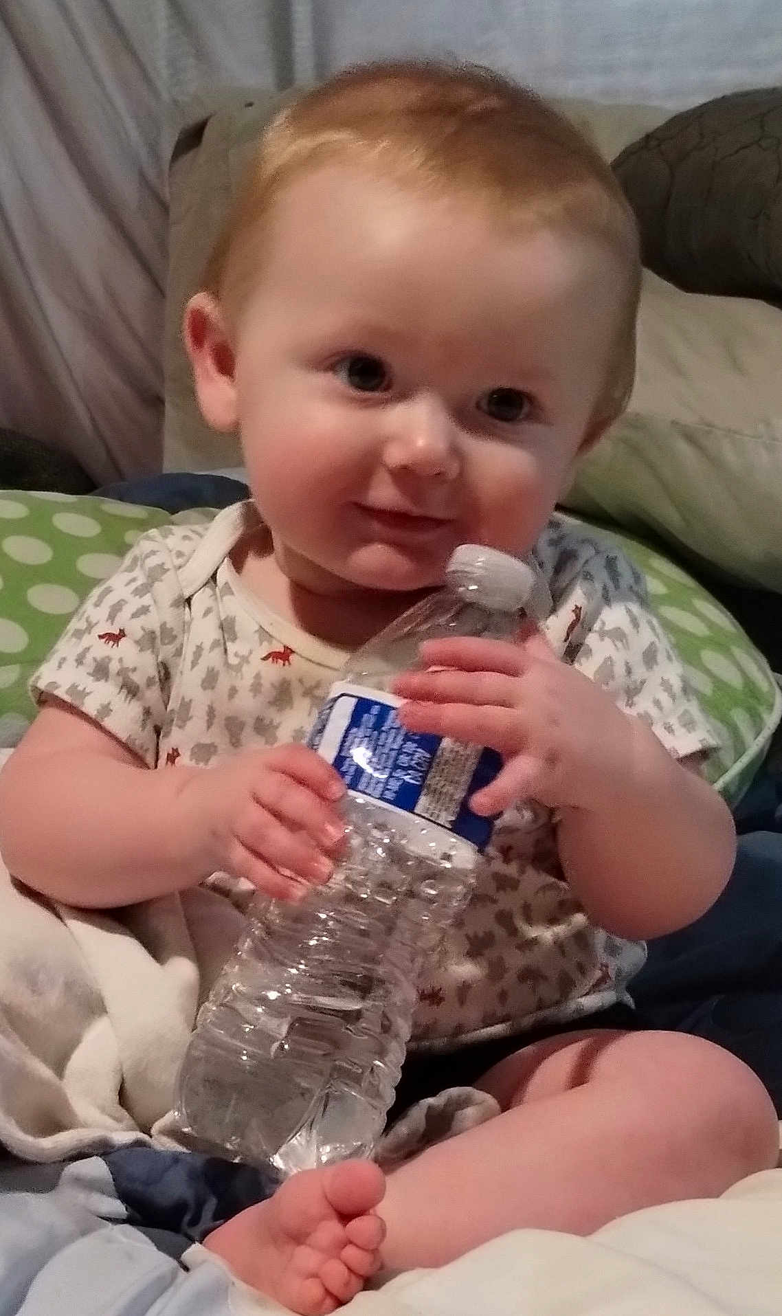 Jeremiah joined the competition — help win amazing prizes! baby, infant, water_bottle, cute, smiling, red_hair, sitting, blanket, pillow, indoor, child, holding, foot, clothing, onesie, person, skin, hand, face, relaxing